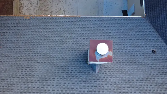 Drone photo looking down on a chimney chase cap on an asphalt shingle roof